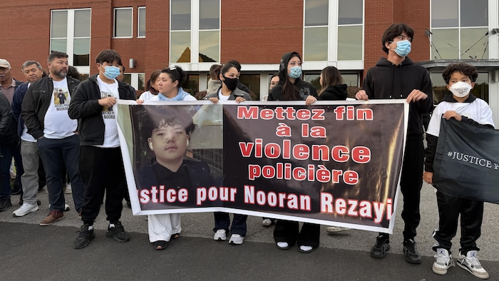 Des manifestants masqués tiennent une banderole réclamant la fin de la violence policière pour Nooran Rezayi.