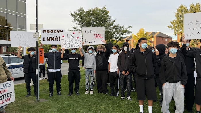 Des jeunes personnes masquées brandissent des pancartes réclamant justice sur une pelouse.