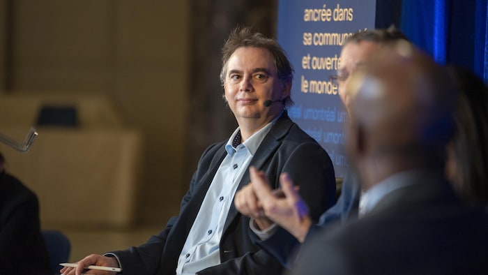 Un professeur conférencier, micro à la bouche, à l'écoute d'autres conférenciers. 