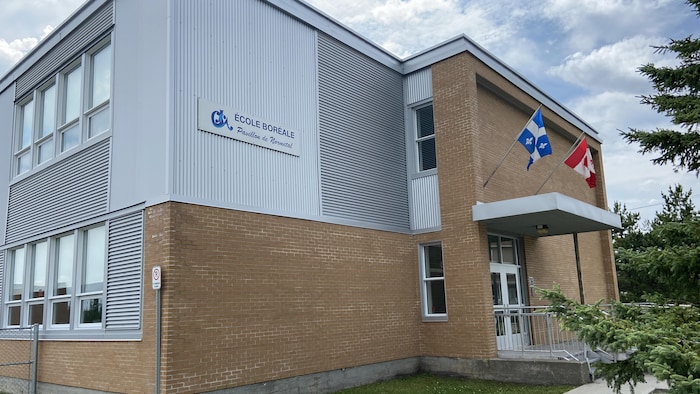Photo extérieure de l'école Boréale de Normétal, avec un drapeau du Québec et un drapeau du Canada au-dessus de la porte d'entrée.