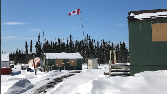 Un drapeau canadien flotte par-dessus des maisons en bois dans un paysage hivernal.