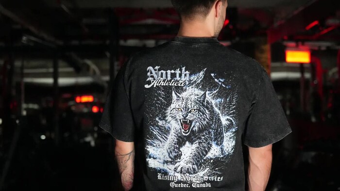 Un homme de dos porte un t-shirt où apparait un dessin de lynx.