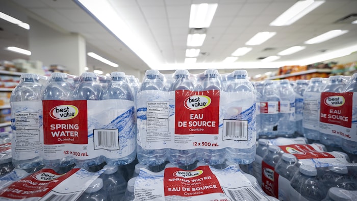 Des emballages de douze de bouteilles d'eau empilés les uns sur les autres dans une épicerie.