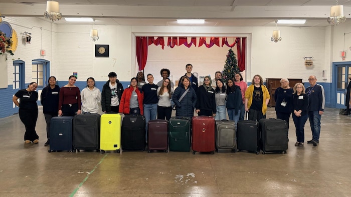 Un groupe de personnes posent pour la photo derrière une dizaine de valises fermées.
