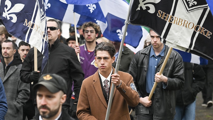 Des hommes de Nouvelle Alliance, l'air sérieux, brandissent des drapeaux de leur organisation à Montréal, le 19 mai 2025.