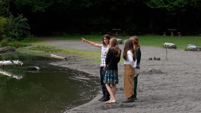 Quatre jeunes femmes rassemblées sur la berge d'un lac bordé d'arbres.