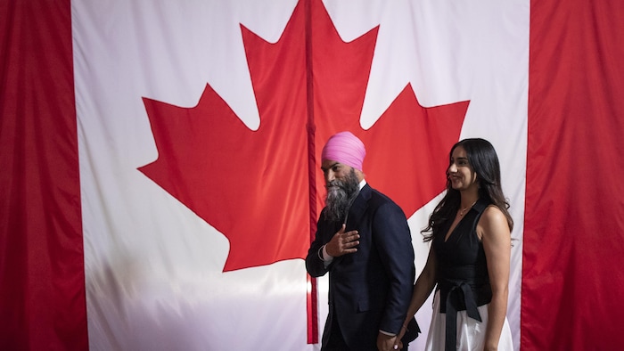 Jagmeet Singh et sa femme devant un expansive drapeau canadien.