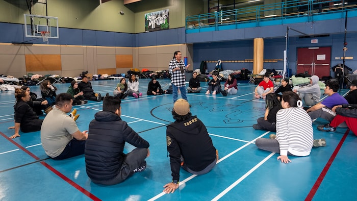 Les jeunes écoutent en cercle dans un gymnase.