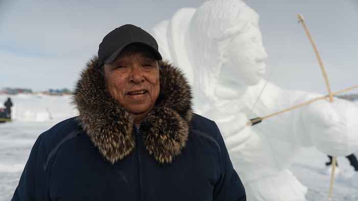  Peter Ittukallak devant sa sculpture sourit à la caméra.