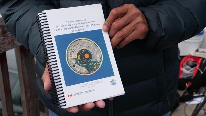 Une personne tient dans ses mains une copie de l'accord sur les revendications territoriales du Nunavut.