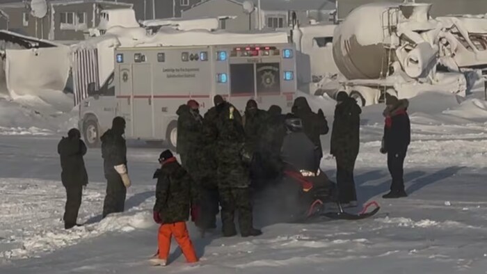 Un groupe de personnes sont attroupées autour d'un membre des Forces armées canadiennes blessé après un atterrissage brutal en parachute à Cambridge Bay, au Nunavut, le 3 mars 2026.
