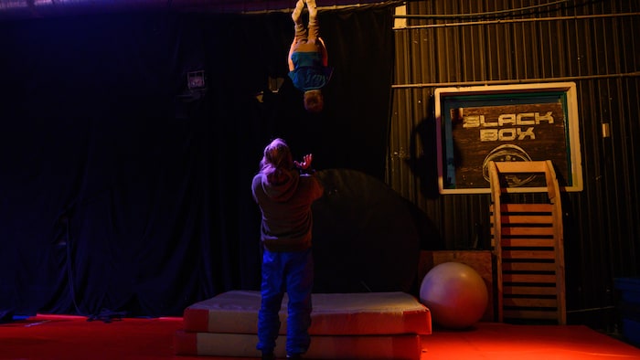Un enfant effectue une culbute dans les airs pendant qu'un homme tend ses mains pour le rattraper.