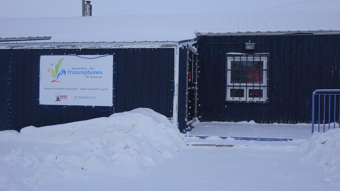 Façade d'un édifice en hiver avec une grande affiche indiquant l'Association des francophones d'Iqaluit.