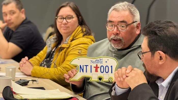Un homme assis à côté de plusieurs personnes tient une plaque d'immatriculation en forme d'ours polaire, à Iqaluit, au Nunavut, le 20 mai 2025.