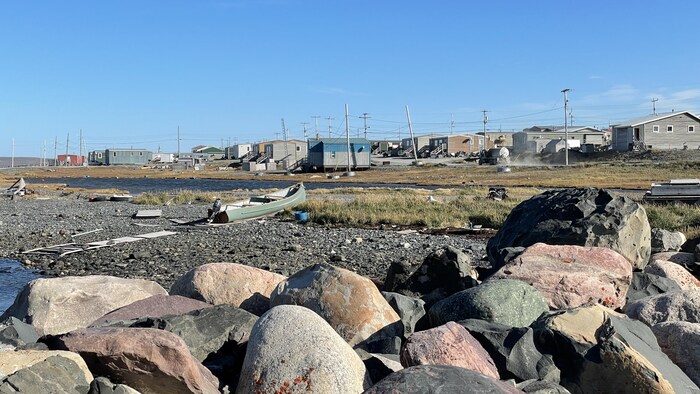 Une barque est posée dans le sable près de l'eau devant des maisons de Sanikiluaq.