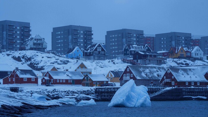 Un petit iceberg flotte près de la berge, devant des habitations.
