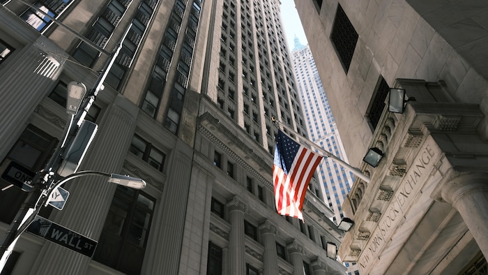 La façade du New York Stock Exchange, à New York, avec un drapeau américain qui flotte.