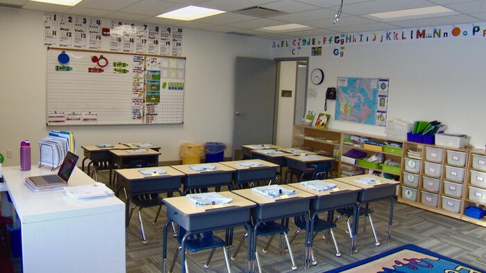 Une salle de classe vide avec une quinzaine de bureaux en rangé.