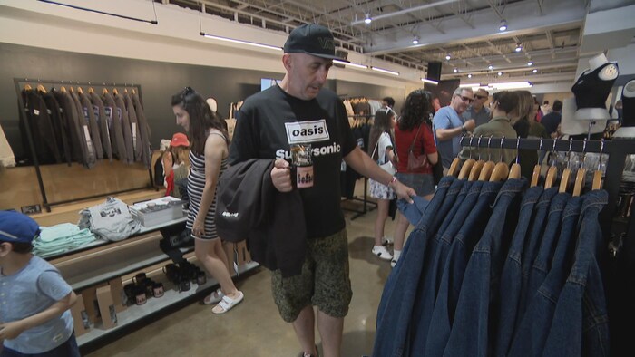 Un homme regarde des blousons en jean, une tasse à la main.