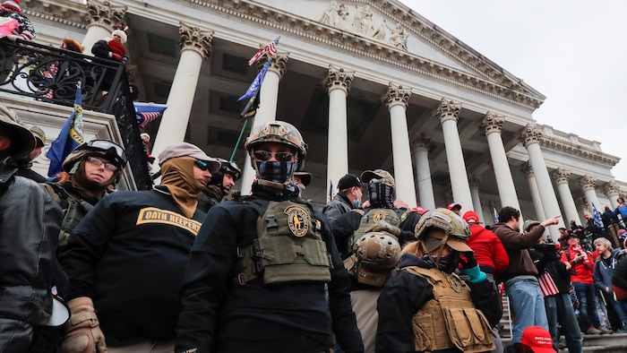 Des membres du groupes sur les marches du Capitole habillés avec des vêtements de combat et des casques.