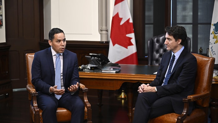 Deux hommes assis dans des fauteuils en cuir. L'un parle, et l'autre (Justin Trudeau) l'écoute et le regarde. 
