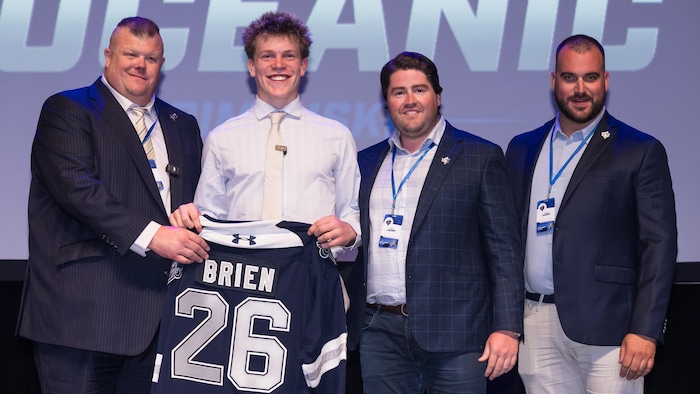 Un jeune joueur tenant un chandail de hockey avec son nom.