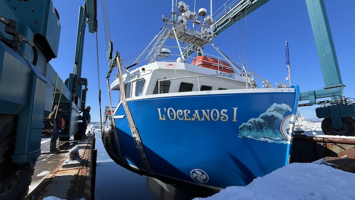 Le bateau L'Océanos I est soulevé par le ber cavalier au-dessus d'un quai enneigé sous un ciel dégagé.