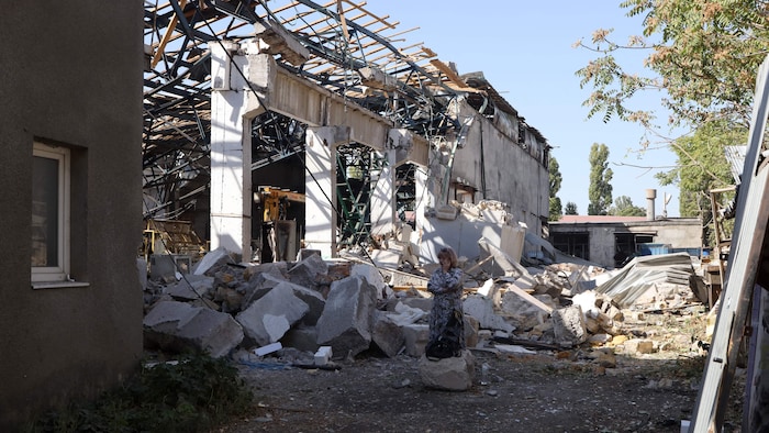 Une femme au téléphone à côté des débris d'un édifice dont les murs et le toit ont été soufflés. 
