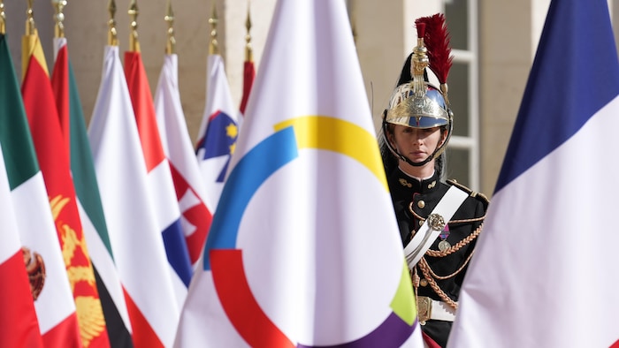 Un garde d'honneur est debout entre un drapeau de l'Organisation internationale de la Francophonie et un drapeau français à Villers-Cotterêts, en France, le 4 octobre 2024, au Sommet de la Francophonie.