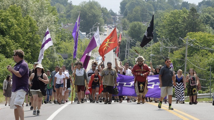 Des Mohawks de Kanesatake marchent dans une rue en brandissant des drapeaux. 