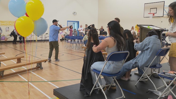 Deux petites filles se font couper les cheveux dans un grand gymnase.