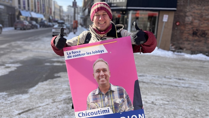 Olivier Dion tient une pancarte électorale à son effigie.