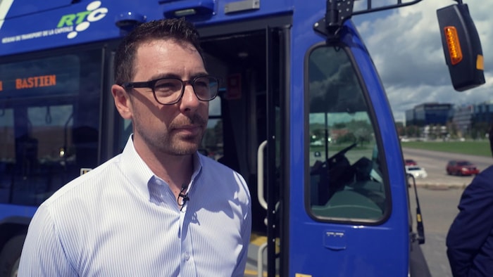 Olivier Pignac-Robitaille accorde une entrevue devant un autobus.