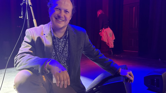 Un homme souriant sur un stage éclairé rouge et bleu.