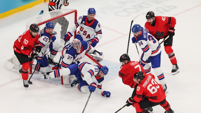 Le joueur canadien Brad Marchand a la rondelle au bout de son bâton devant le filet tandis que des joueurs américains plongent devant lui.