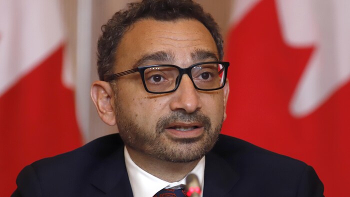 عمر الغبرا متحدثاً في مؤتمر صحفي وخلفه أعلام كندية.