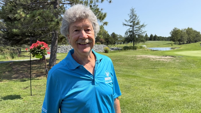 Michel Paiement pose pour la caméra en souriant sur un terrain de golf.