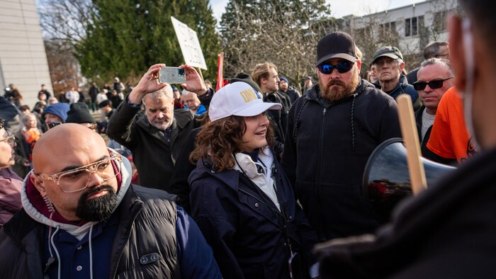 Dallas Brodie entourée de deux gardes de sécurité et encerclée par de nombreux manifestants.