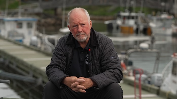 Un homme assis sur un quai devant des bateaux de pêche.
