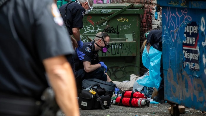 Des ambulanciers aident une personne allongée au sol dans une ruelle.
