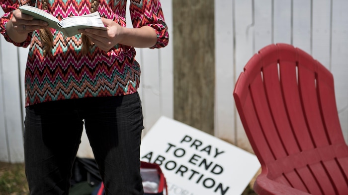 Une femme, dont on ne voit pas la tête, lit la Bible près d'une pancarte qui dit : « Priez pour mettre un terme à l'avortement ».