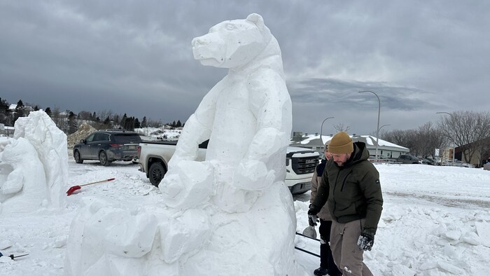 Un père et son fils marchent autour d'une sculpture d'un ours en neige.