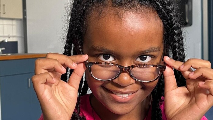 Une fillette souriante avec une paire de lunettes qu'elle tient des deux côtés.