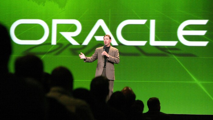 Le PDG d'Oracle, Larry Ellison, livre un discours sur une scène devant le logo de son entreprise.