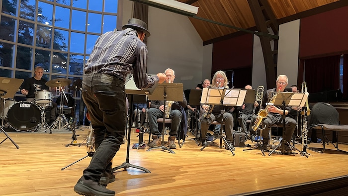 Robert-Siméon est de dos, sur scène, il dirige les musiciens qui sont à l'oeuvre.