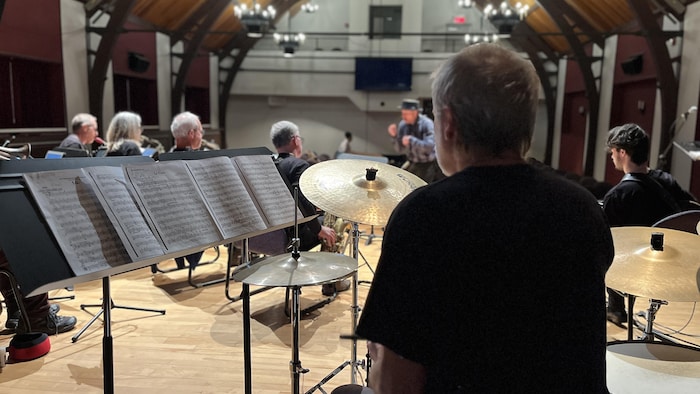 Le batteur est de dos, devant lui, d'autres musiciens sur scène.