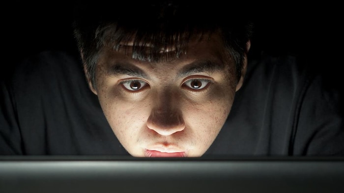Un adolescent devant l'écran d'un ordinateur portable dans l'obscurité.