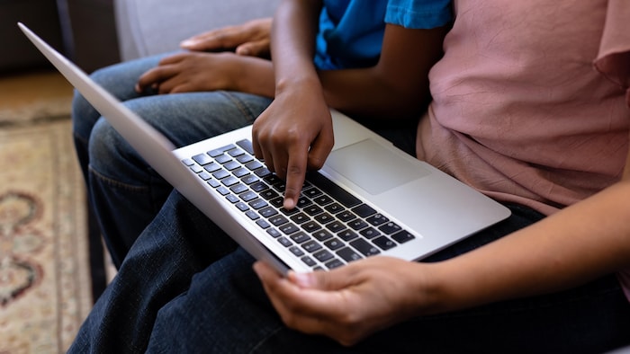 Couple mixte de personnes âgées avec leurs petits-enfants, profitant de leur temps à la maison, assis sur un canapé, utilisant un ordinateur portable.