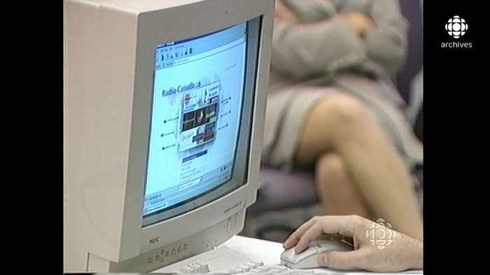 Gros plan sur un écran qui montre le site web de Radio-Canada. Une main tient une souris d'ordinateur. 