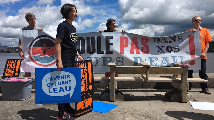 Quatre personnes avec des pancartes sur lesquelles on peut lire des slogans comme 'Coule pas chez nous'.